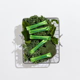 Basket filled with green vegetables and 'Daily Greens' packages on a white background