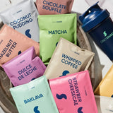 Assorted DailyShake protein powder packets in various flavors with a shaker bottle.